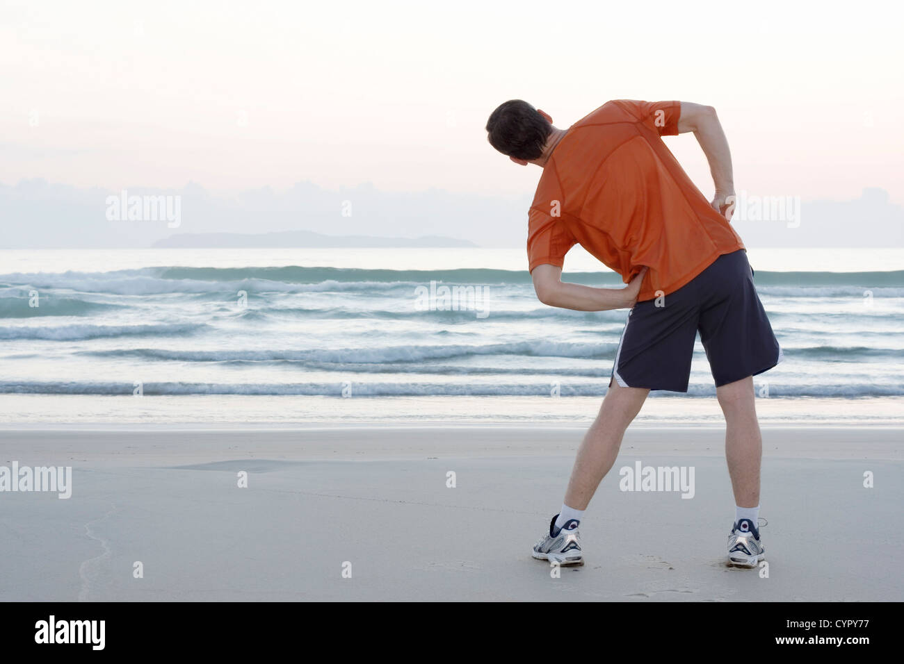 Runner faisant des exercices d'étirement sur une plage tôt le matin Banque D'Images