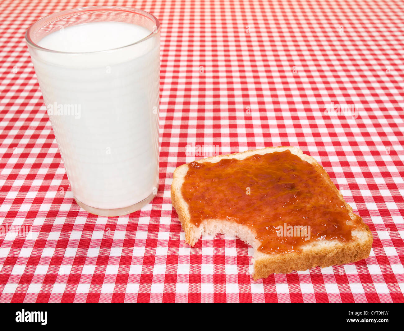 Un verre de lait et d'un toast avec de la confiture, propagation d'un morceau manquant. Banque D'Images