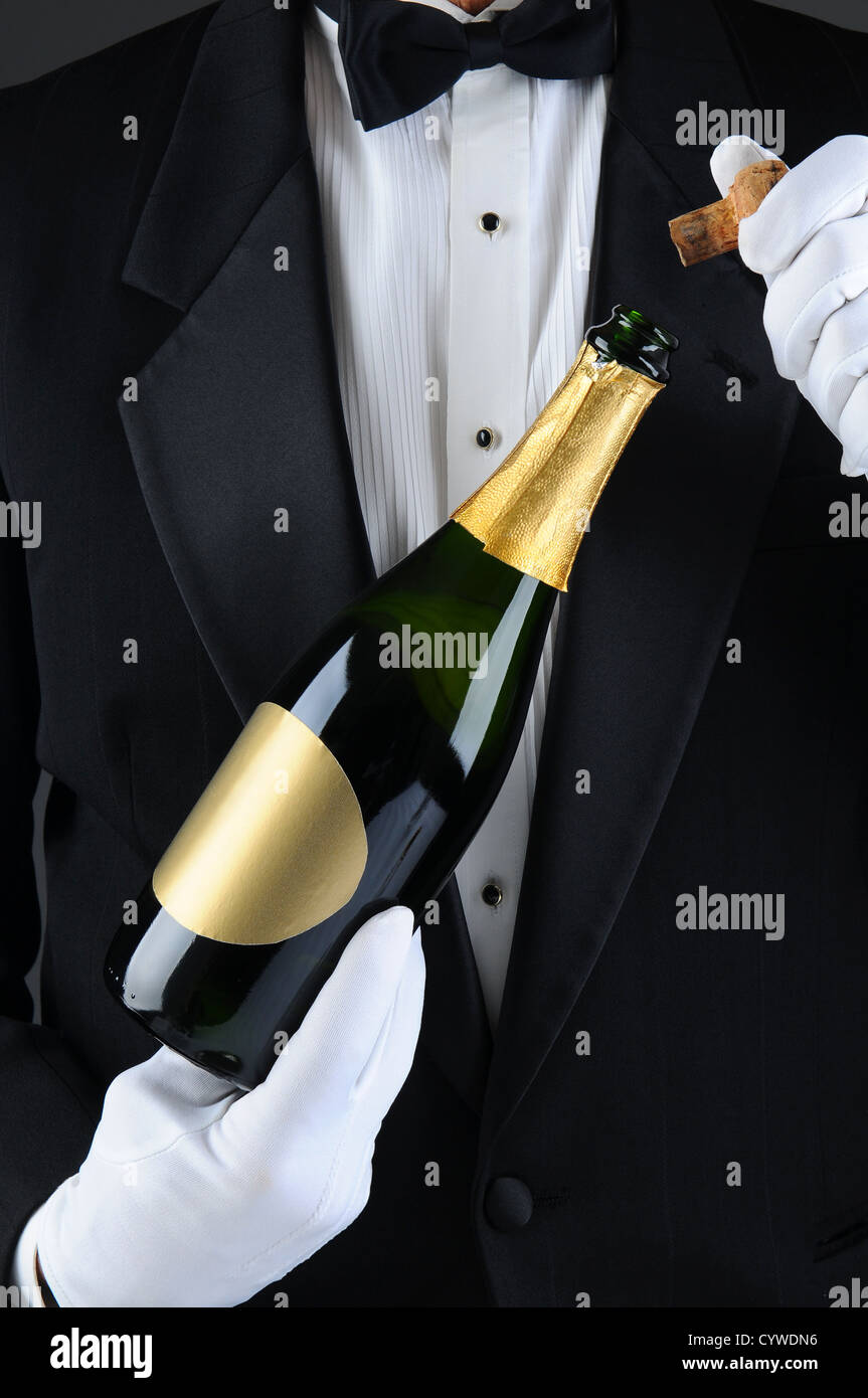 Gros plan du sommelier, déboucher une bouteille de champagne. L'homme est méconnaissable vêtu d'un smoking et gants blancs. Format vertical. Banque D'Images