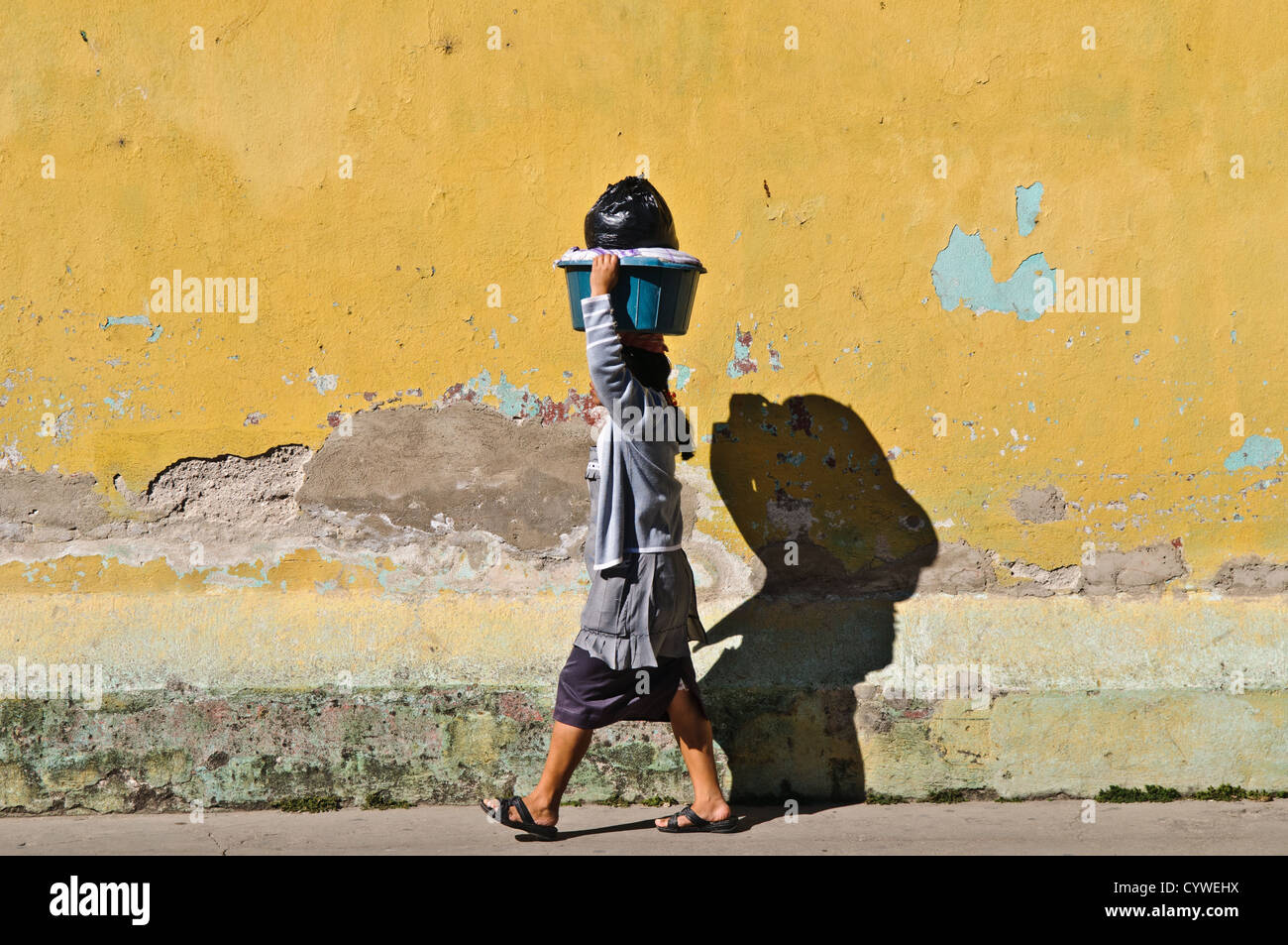 ANTIGUA GUATEMALA, Guatemala — Une femme d’Antigua, Guatemala, marche le long d’une rue contre le mur peint en jaune d’un bâtiment colonial avec un panier en équilibre sur la tête. Banque D'Images