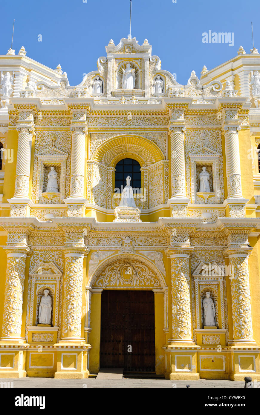 Iglesia de la Merced entrée principale Antigua Guatemala // ANTIGUA, Guatemala — entrée principale de l'extérieur jaune et blanc distinctif et orné de l'Iglesia y Convento de Nuestra Señora de la Merced dans le centre-ville d'Antigua, Guatemala. La façade est richement ornée de stuc blanc complexe, y compris des statues de saints, des colonnes torsadées et des motifs décoratifs, le tout placé contre les murs jaunes vibrants. Banque D'Images