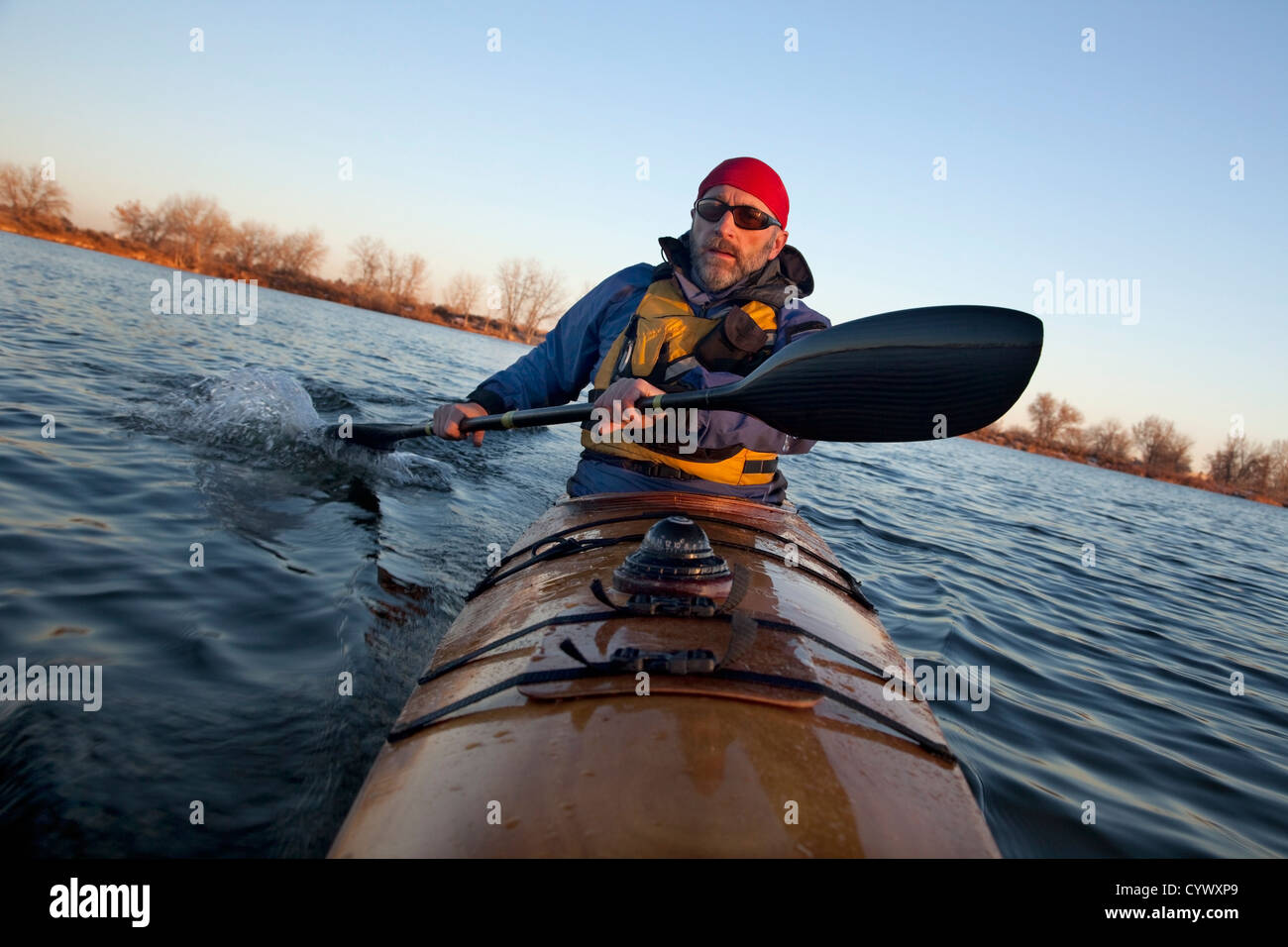 L'exercice de pagayeur mâles matures (en tournant à l'aide de bateau de course de la gouverne avec son aile pagaie en fibre de carbone) en kayak de mer en bois Banque D'Images