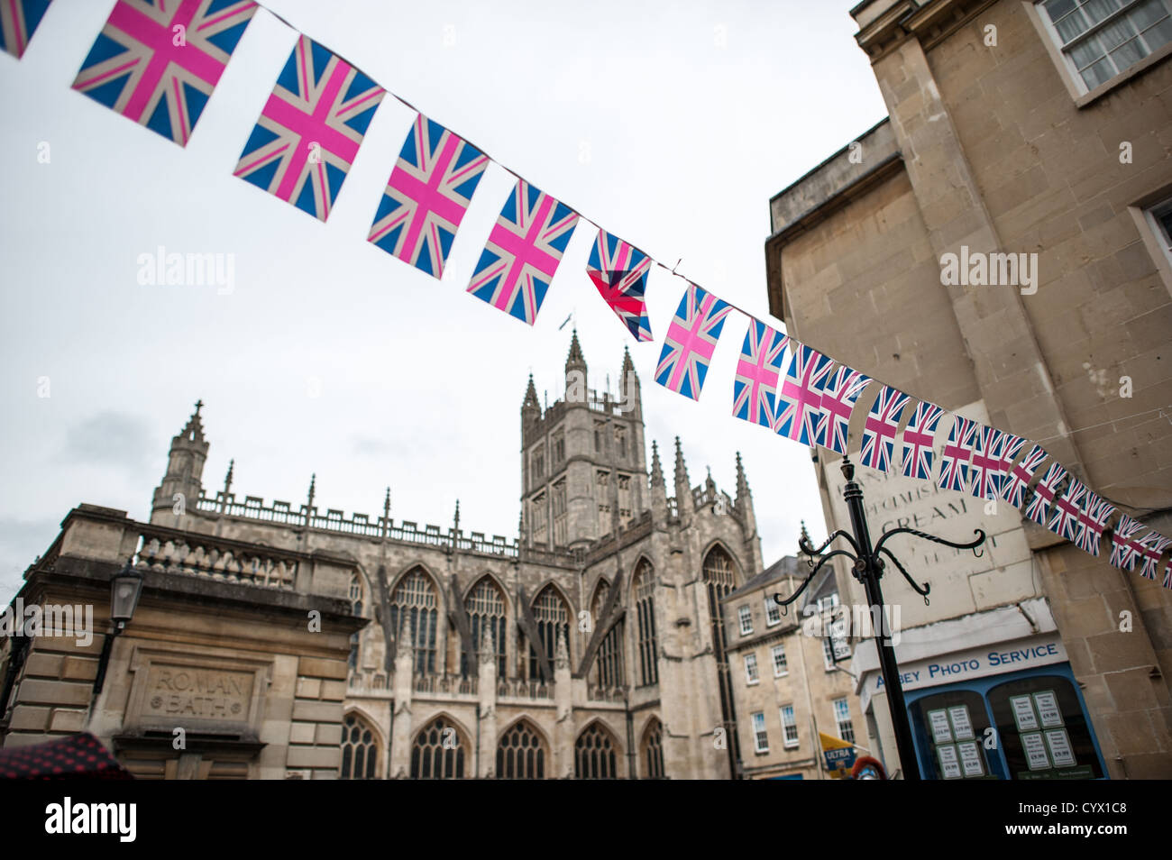 BATH, Somerset, Royaume-Uni — la banderole colorée de l'Union Jack s'étend de l'autre côté d'une rue dans la ville historique de Bath, créant une atmosphère festive avec pour toile de fond l'emblématique abbaye de Bath. L'église gothique, officiellement connue sous le nom d'église abbatiale Saint-Pierre et Saint-Paul, domine l'horizon de la ville depuis le XVIe siècle, bien qu'un lieu de culte se trouve sur ce site depuis le VIIIe siècle. Le bâtiment actuel est réputé pour sa voûte en éventail et ses grands vitraux. Bath, site classé au patrimoine mondial de l'UNESCO, est réputé pour ses thermes romains préservés et son architecture géorgienne Banque D'Images