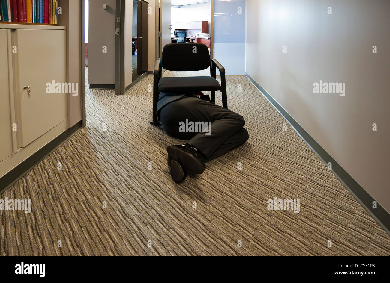 L'homme portant sur le plancher sous une chaise dans un couloir de bureau Banque D'Images