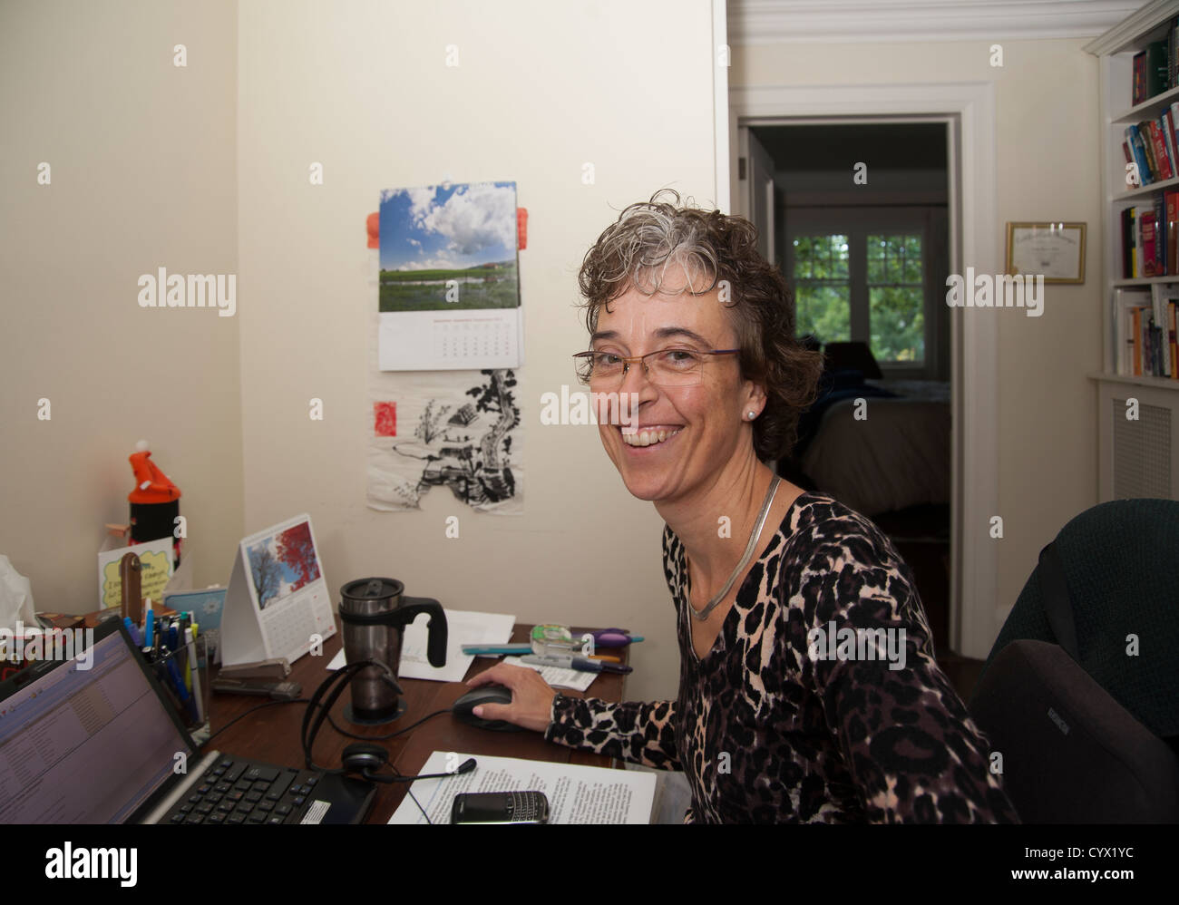 Femme assise à son bureau à domicile, travail à la caméra en souriant Banque D'Images
