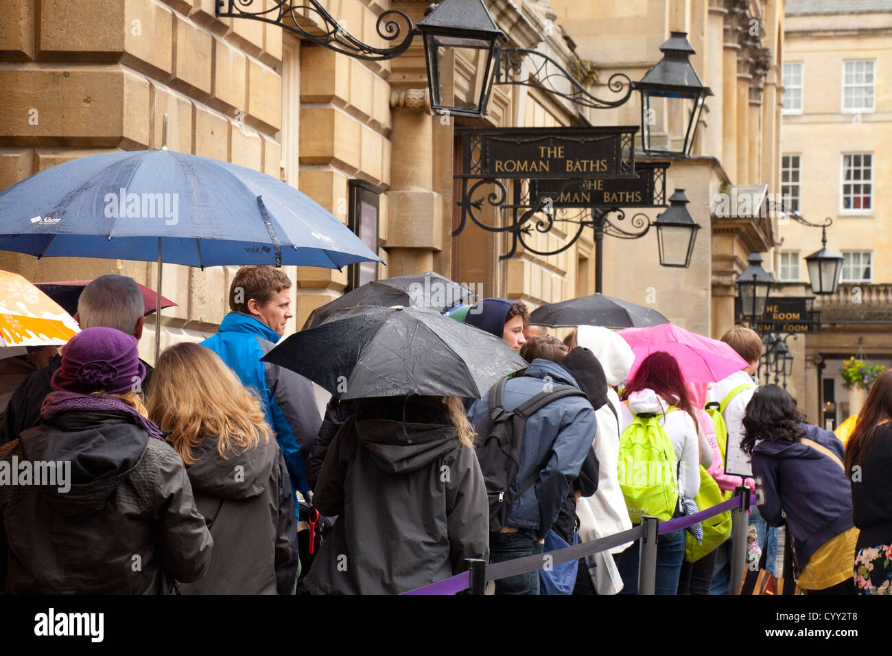 Des foules de gens dans une file d'attente sous la pluie d'entrer dans les bains romains, baignoire Somerset UK Banque D'Images