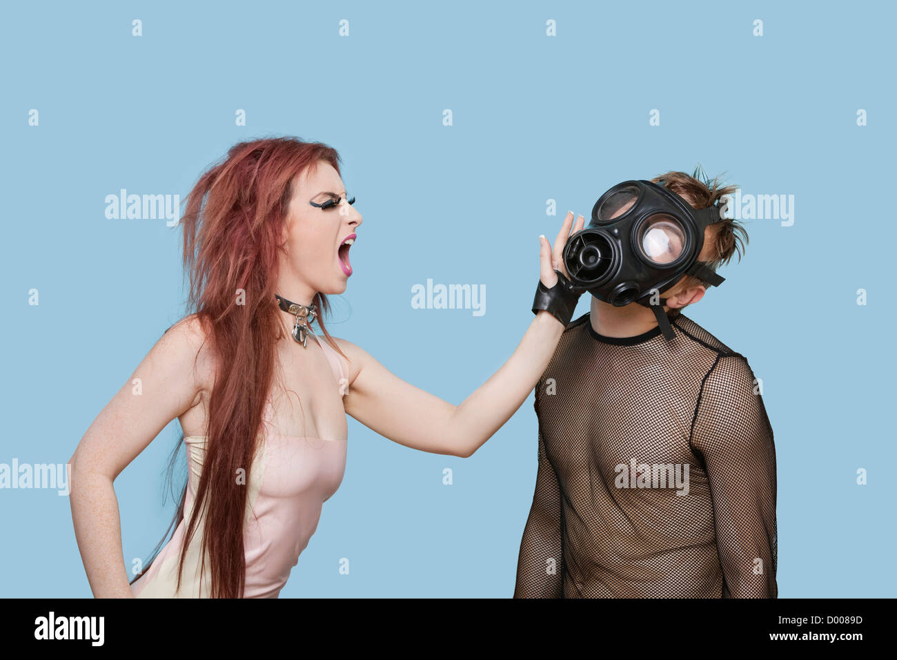 Jeune femme Funky homme gifler en masque à gaz sur fond bleu Banque D'Images
