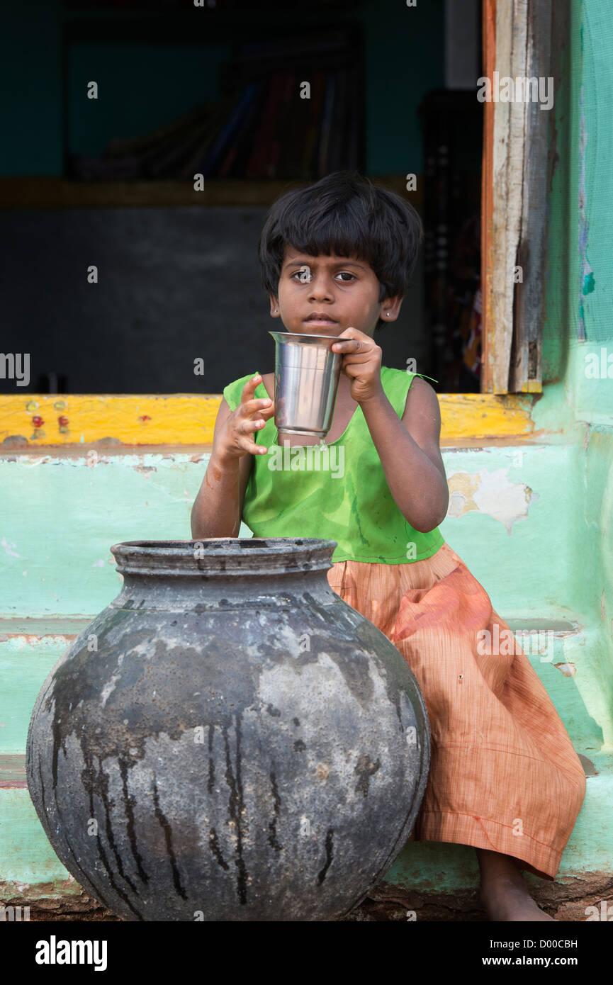 Fille village eau potable d'un pot de terre cuite à l'extérieur d'une maison indienne. L'Andhra Pradesh, Inde Banque D'Images