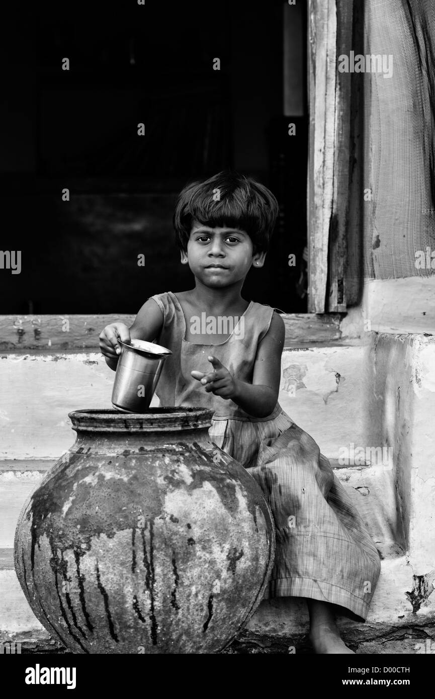 Fille village eau potable d'un pot de terre cuite à l'extérieur d'une maison indienne. L'Andhra Pradesh, Inde. Noir et blanc. Banque D'Images