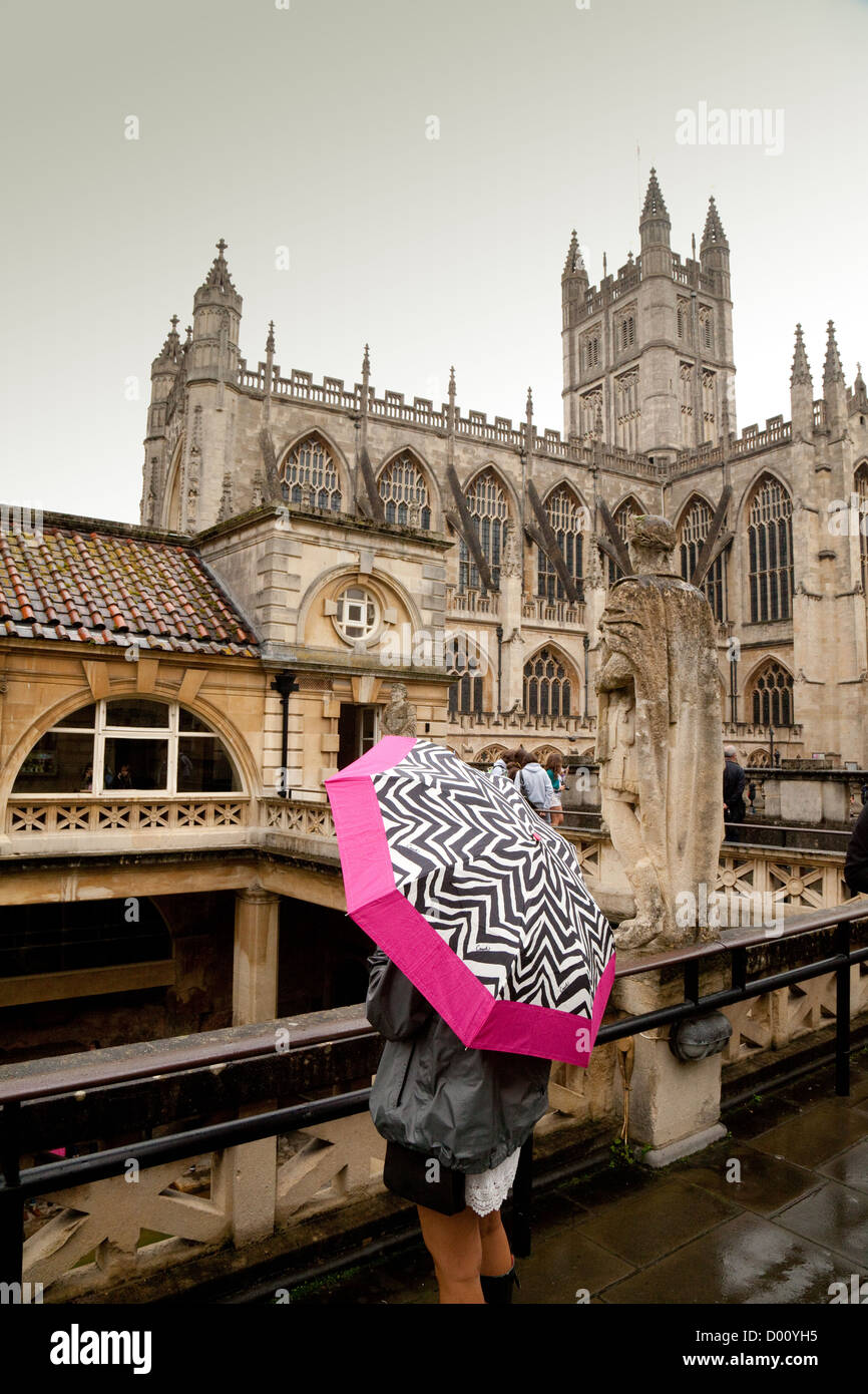 Un touriste aux bains romains de la pluie à l'abbaye dans l'arrière-plan ; bain Somerset UK Banque D'Images