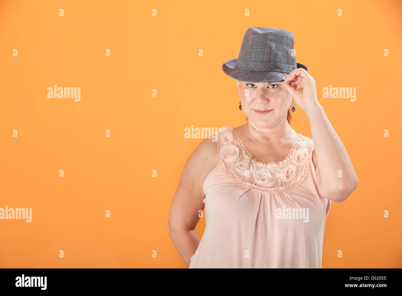 Middle-aged woman sur fond orange trucs son chapeau Banque D'Images
