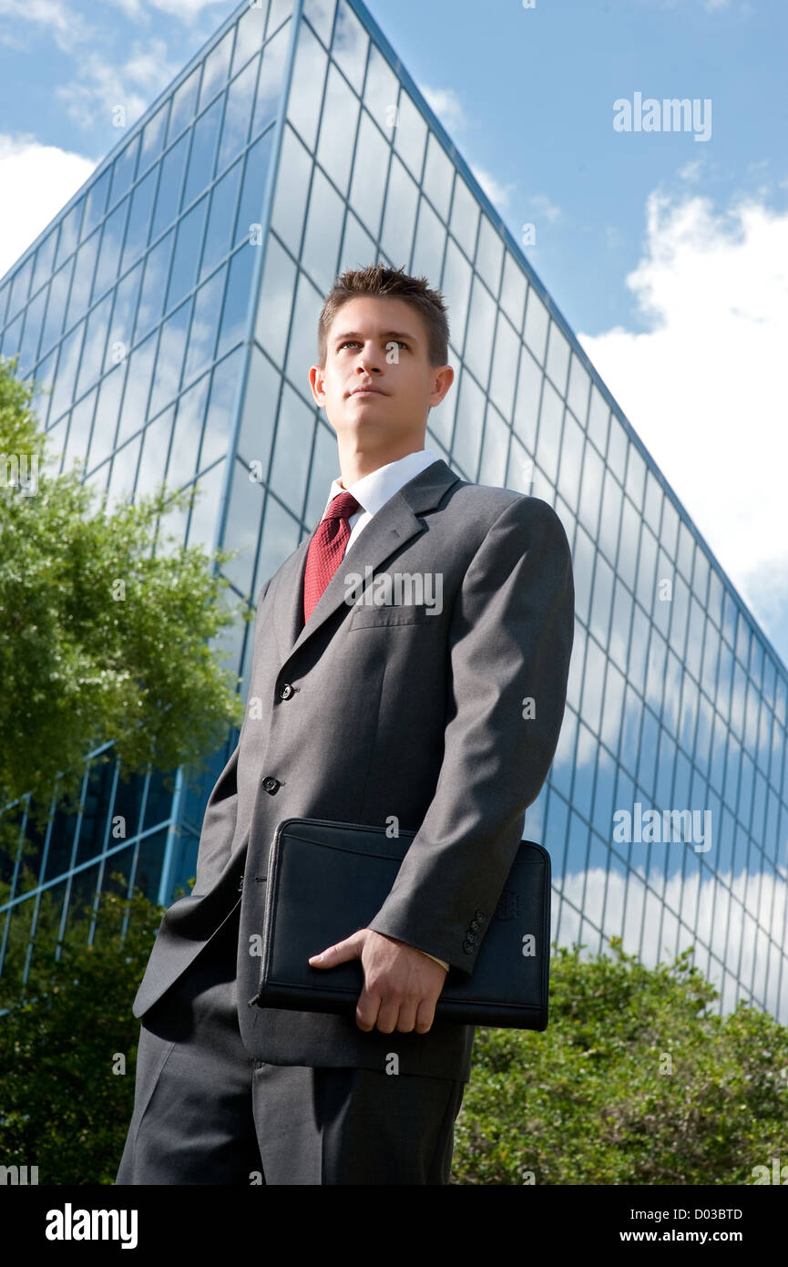 Un jeune homme d'affaires qui a du succès dans sa suite porte une mallette devant une tour moderne. Banque D'Images