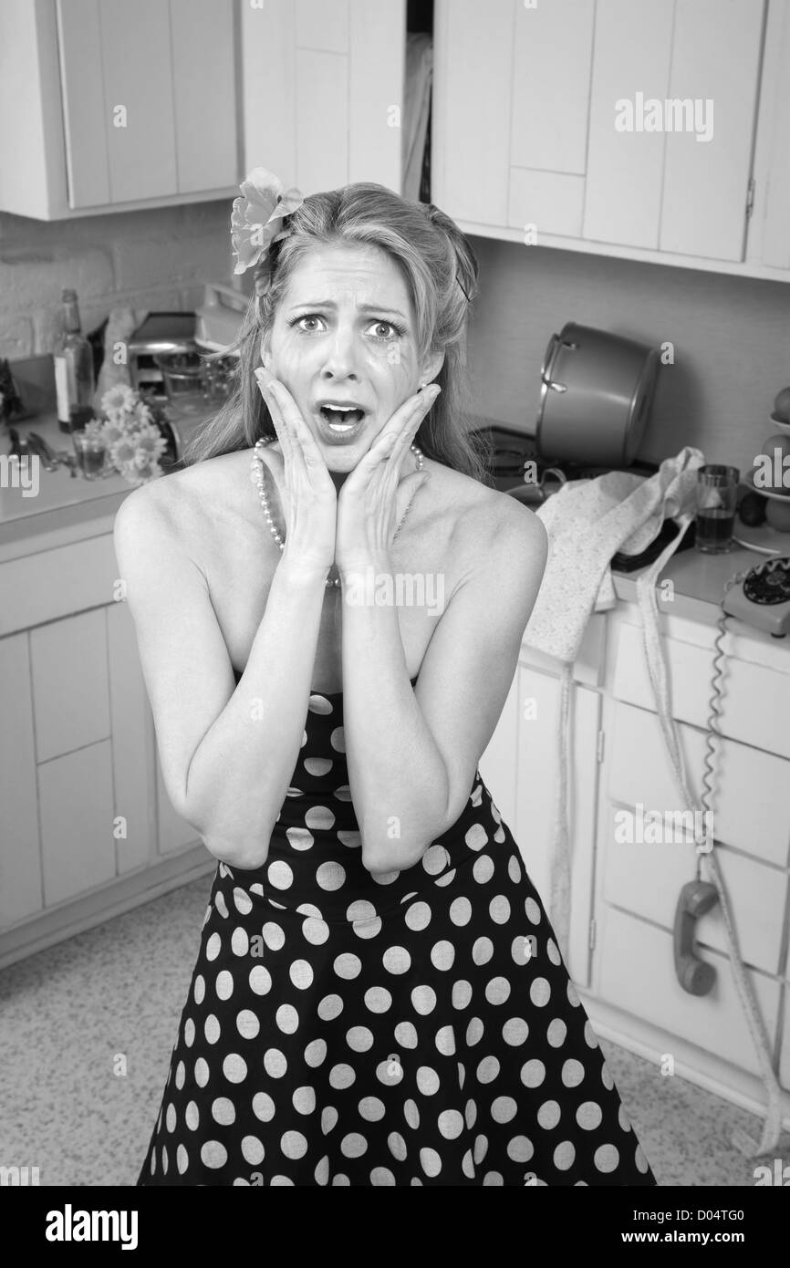 Choqué Caucasian woman en cuisine de style rétro en désordre avec les mains sur le visage Banque D'Images