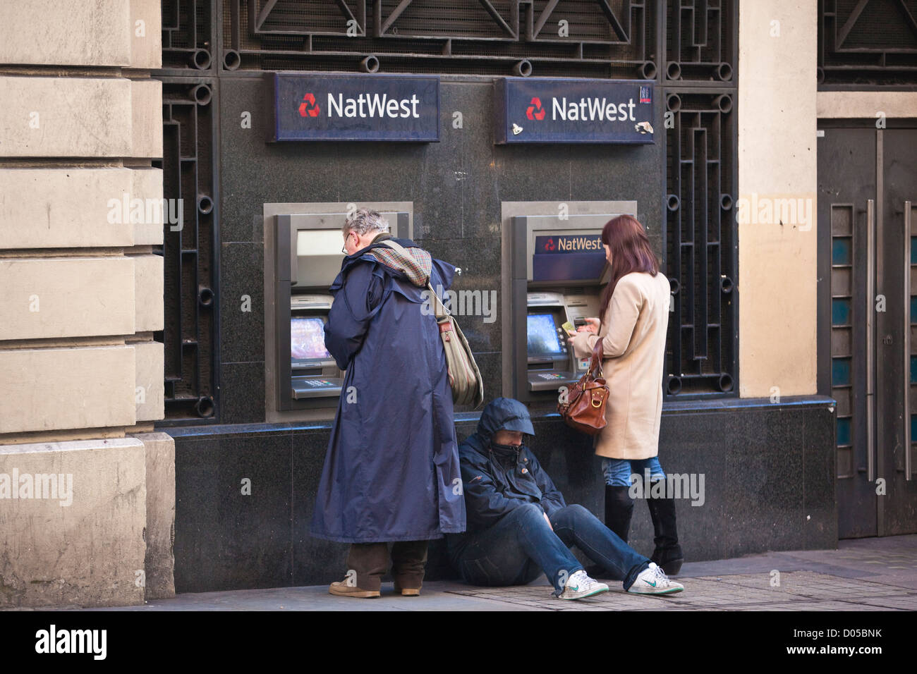 Les gens le retrait d'argent d'un distributeur de billets à l'extérieur de la banque NatWest tandis qu'un homme est assis à mendier, à Covent Garden, Londres, UK Banque D'Images