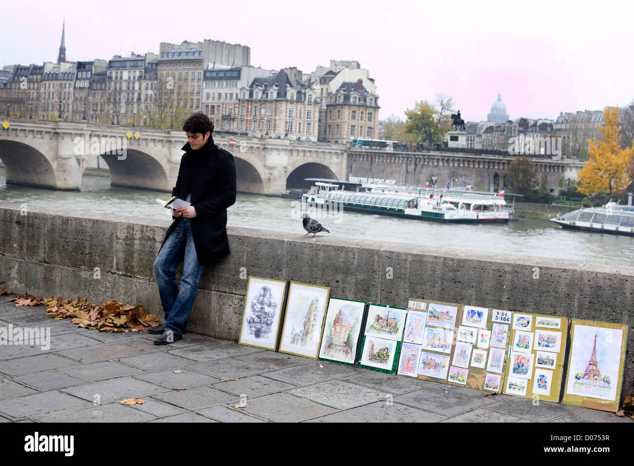 Un homme lit un livre s'en art par la Seine à Paris . D' bateaux de rivière passent dans l'arrière-plan Banque D'Images