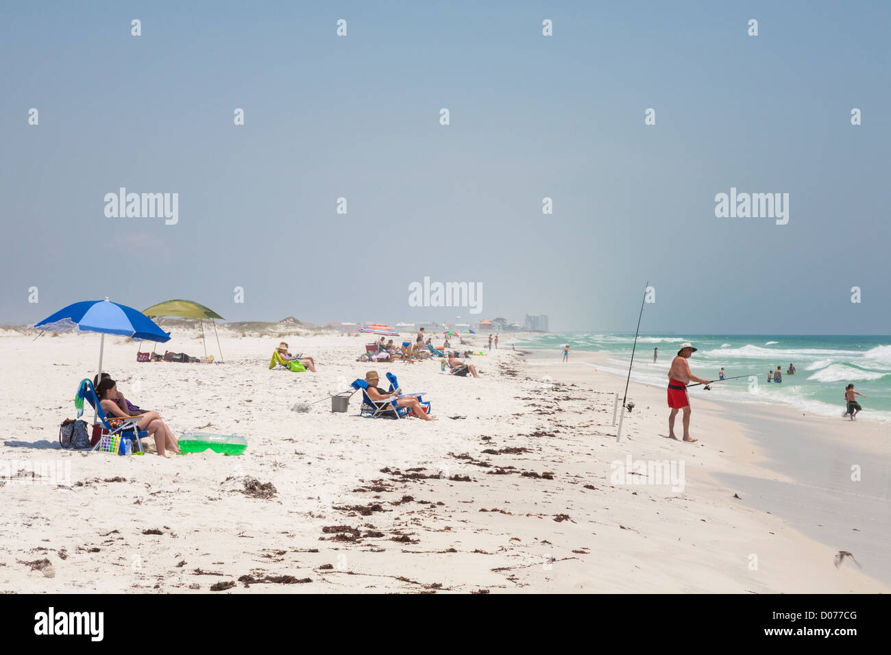 L'homme poissons surf tandis que d'autres le soleil sur plage de sable blanc de Gulf Breeze Banque D'Images