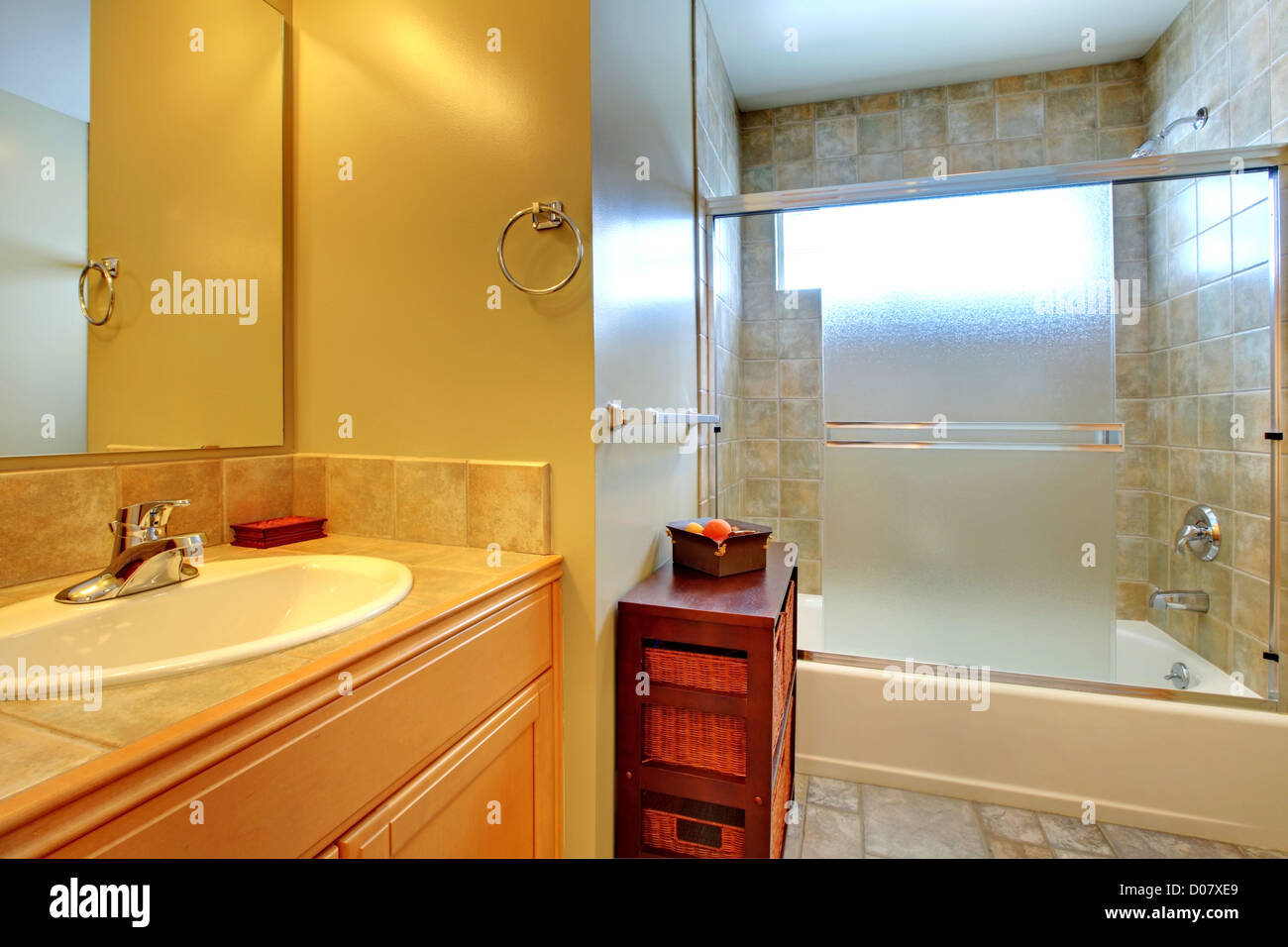 Salle de bains avec baignoire moderne derrière le verre, pierres naturelles, et blanc lavabo dans une armoire en bois. Banque D'Images