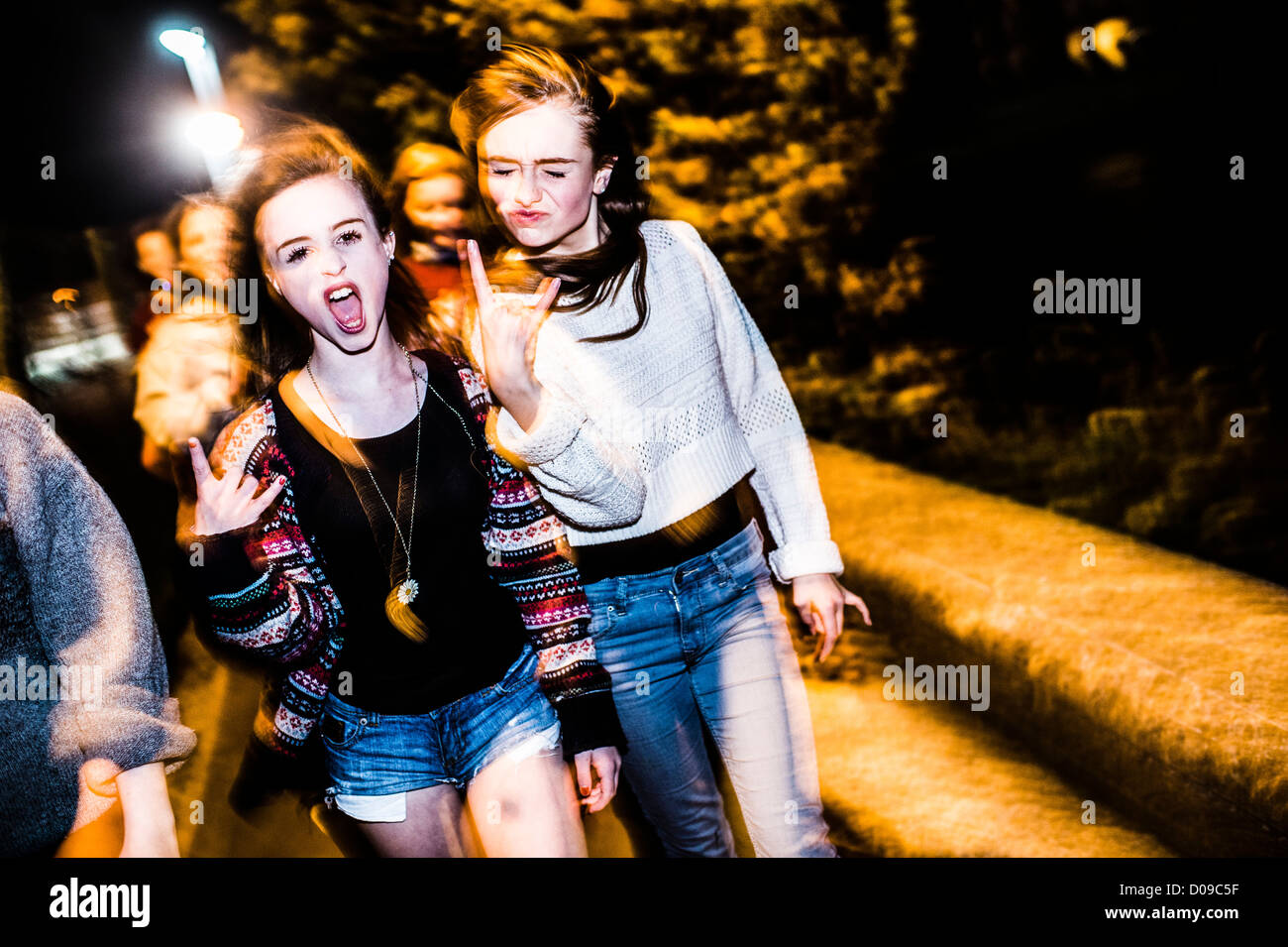 Un groupe de 14 jeunes filles de 15 ans avec des amis s'amuser rire ensemble d'attitude à l'extérieur la nuit UK Banque D'Images