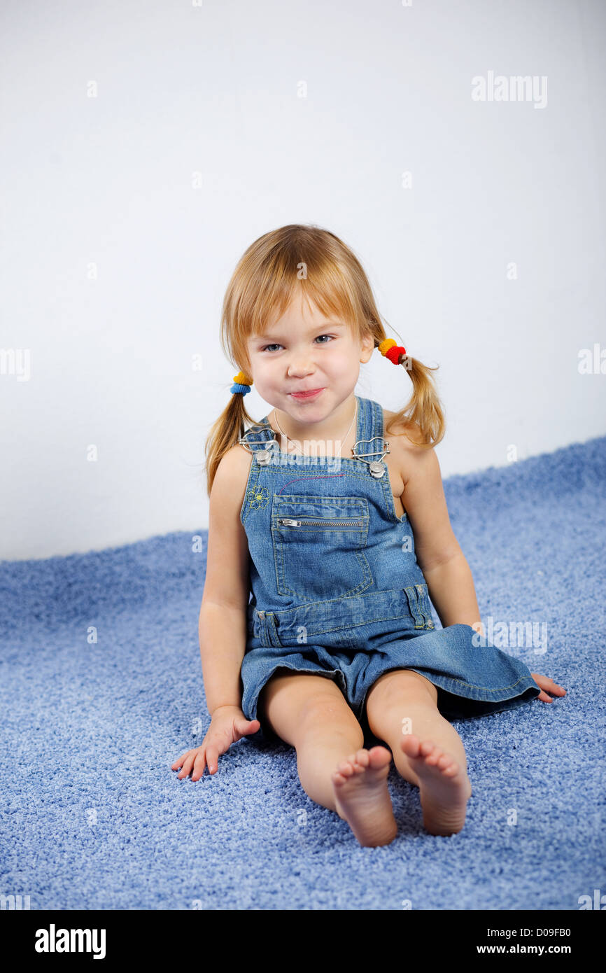 Drôle de petite fille espiègle sur tapis bleu Banque D'Images