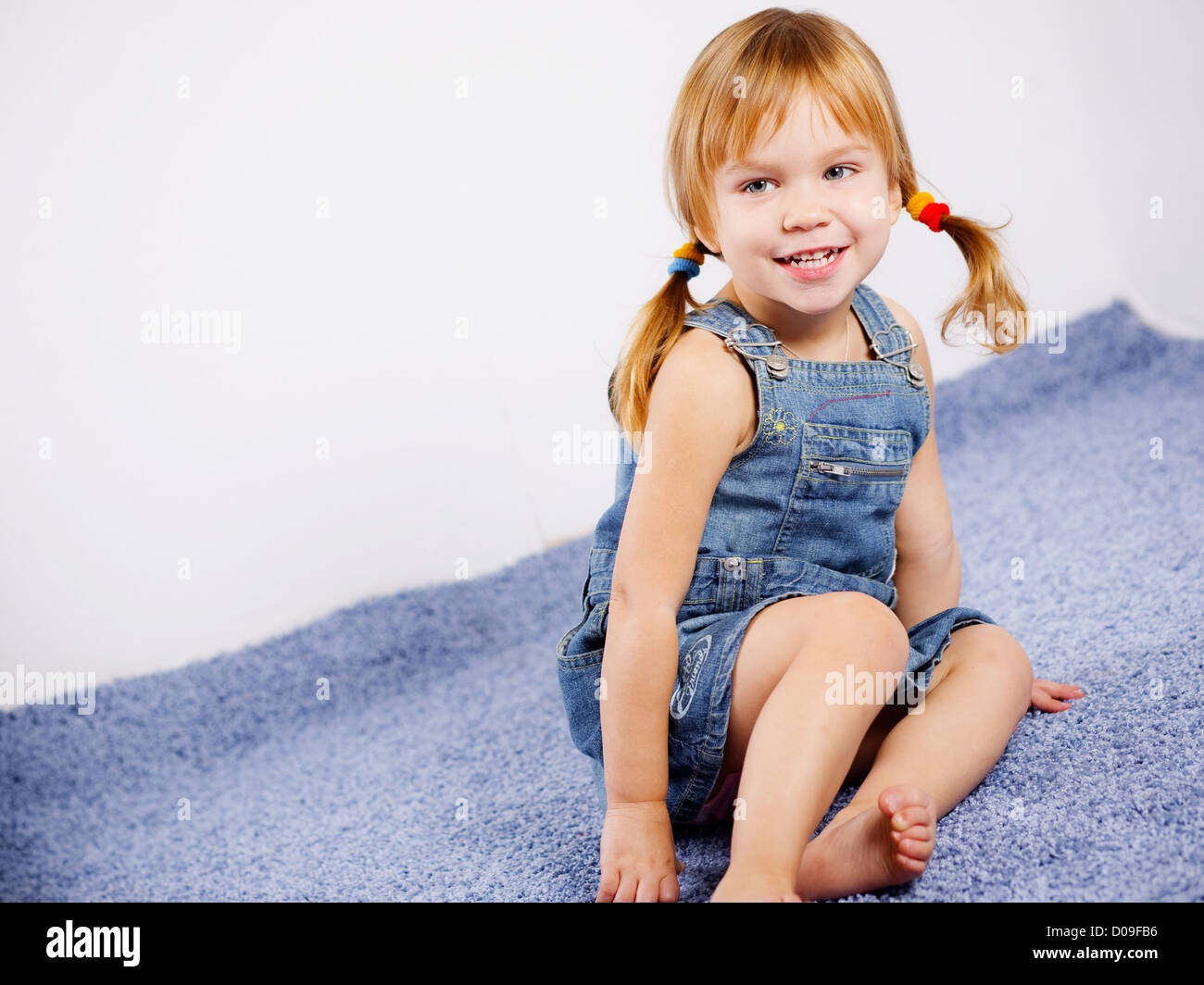 Drôle de petite fille espiègle sur tapis bleu Banque D'Images