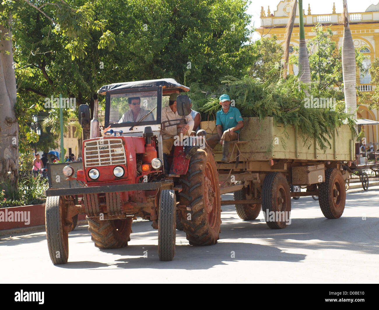 Un vieux tracteur rouge tractant une remorque chargée de verdure tourne un coin dans la vieille ville de Moron cubain coloniale Banque D'Images