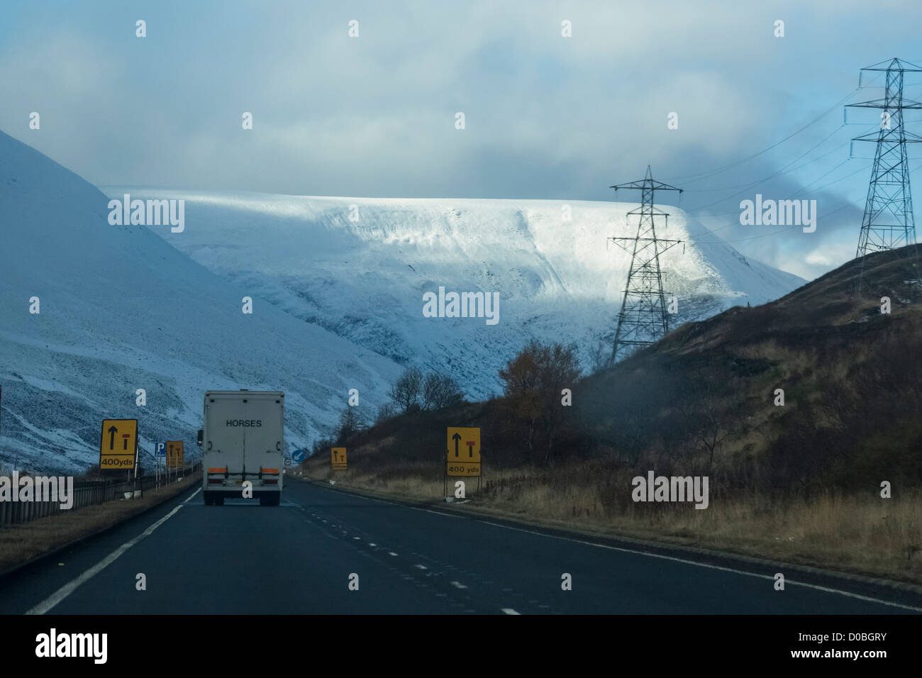 L'approche d'un wagon de travaux routiers sur l'A9 avec des montagnes couvertes de neige dans l'arrière-plan. Banque D'Images
