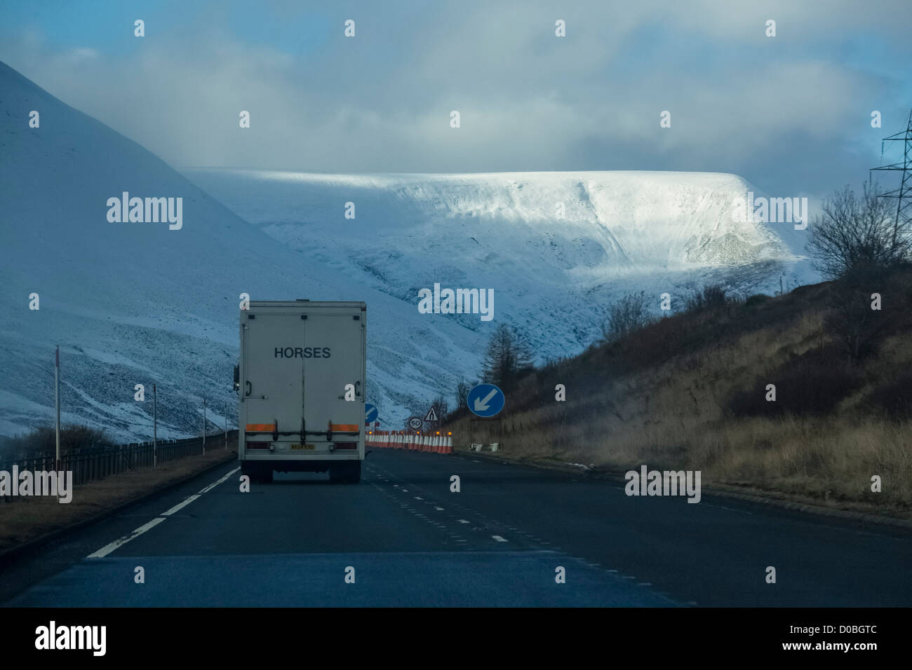 L'approche d'un wagon de travaux routiers sur l'A9 avec des montagnes couvertes de neige dans l'arrière-plan. Banque D'Images