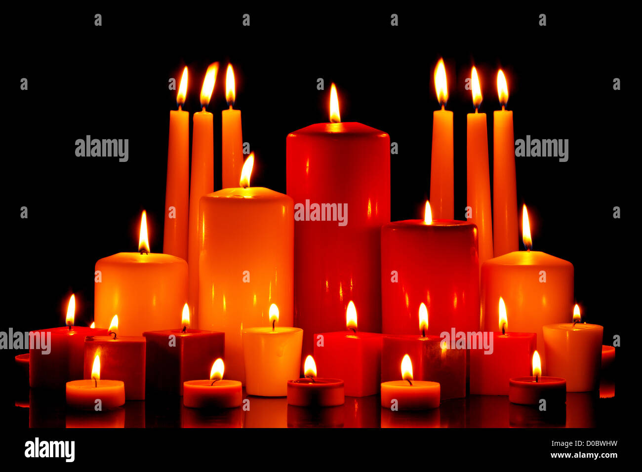 Un grand groupe de taille et de forme mixte de bougies avec des flammes sur un fond noir. Banque D'Images