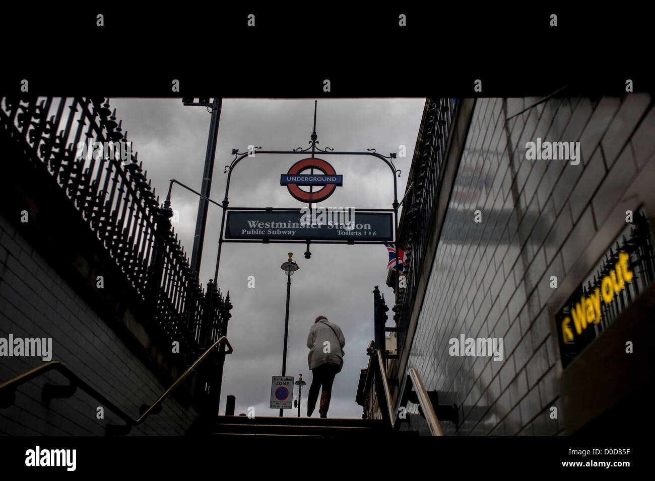 Sur un après-midi d'hiver sombre, avec un ciel gris et monotones, une lumière sort de la station de métro Westminster de banlieue sur Whitehall. L' aller signer et la flèche est écrit en jaune et des points situés dans l'escalier d'où l'homme a atteint le haut des marches, sur le point de poursuivre son voyage le long de la rue ci-dessus. Westminster est une station du métro de Londres dans la ville de Westminster. C'est servi par la Circle, District et de Jubilee. La station est ouverte comme le pont de Westminster le 24 décembre 1868 par la machine à vapeur, chemin de fer du District Métropolitain (MDR) (maintenant la District line) Banque D'Images