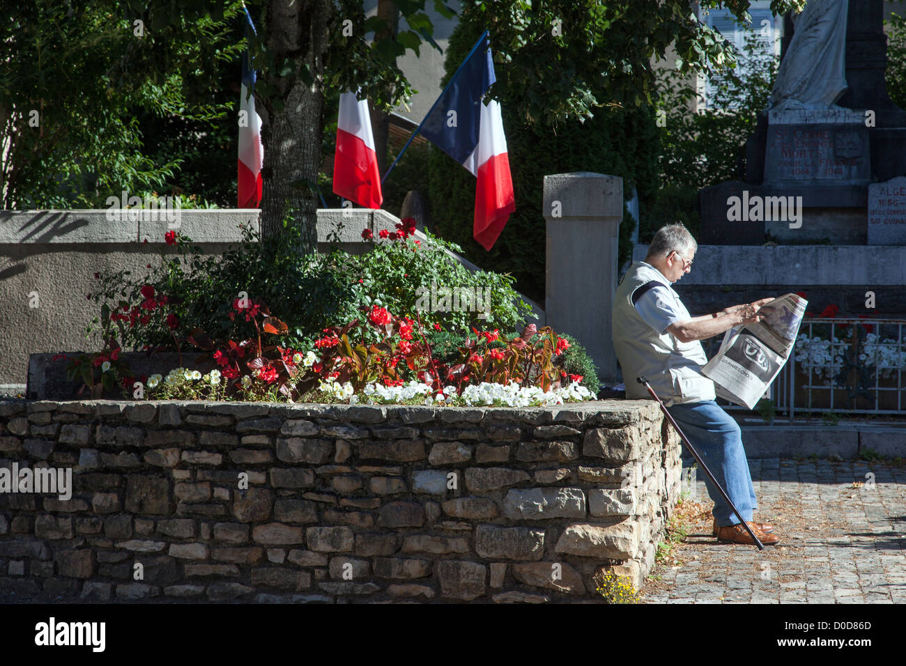 Personne âgée SUR PLACE DU VILLAGE LA LECTURE DE SON JOURNAL DEVANT SON MONUMENT MORTS DE GUERRE drapeaux français SAINT-COME D'OLT NOMMÉ UN Banque D'Images