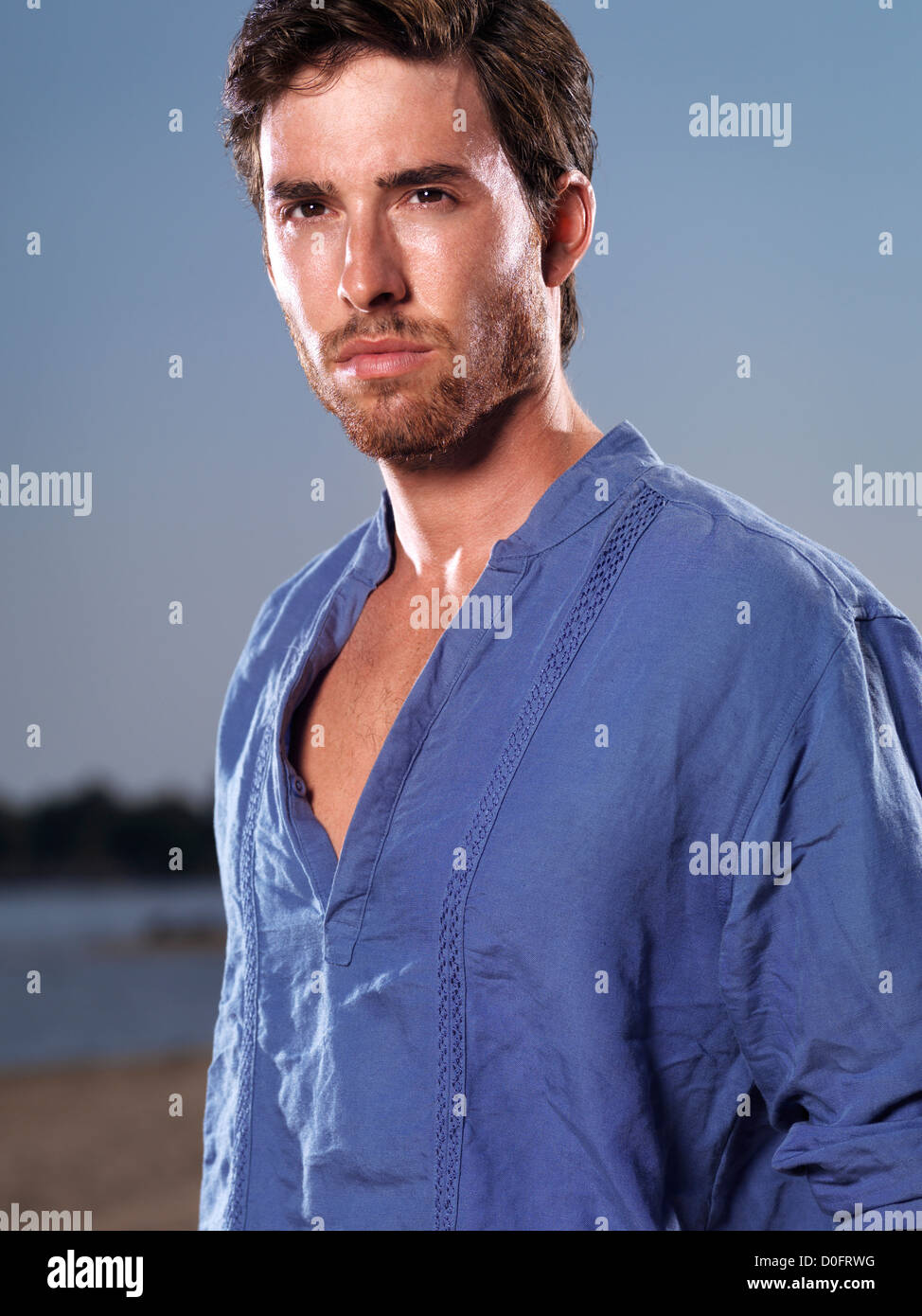 Fashion portrait d'un jeune homme portant une chemise bleue sur fond de ciel bleu à la plage Banque D'Images
