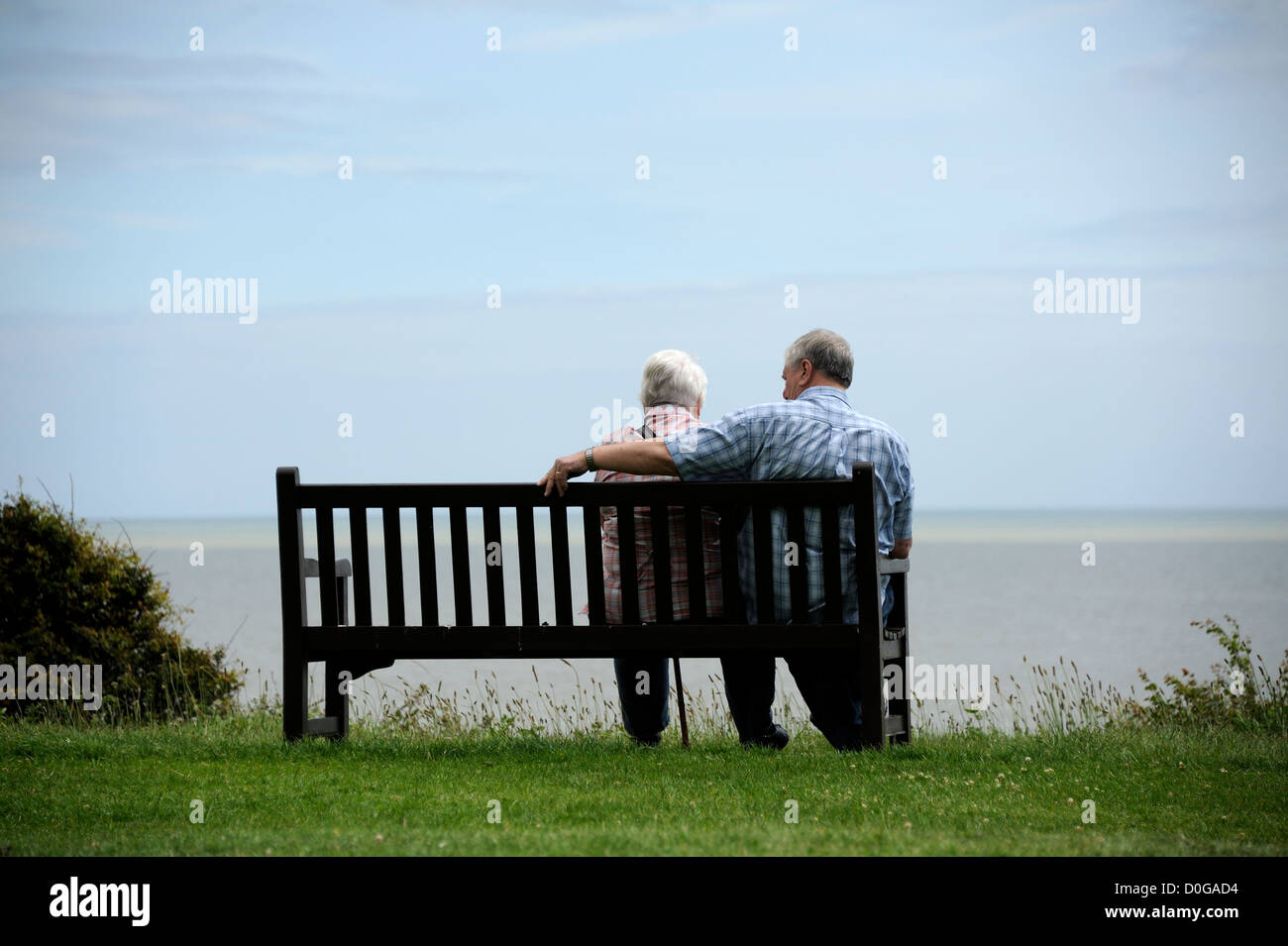 Un couple de personnes âgées regardez vers la mer à partir d'un banc de parc au Royaume-Uni. Banque D'Images