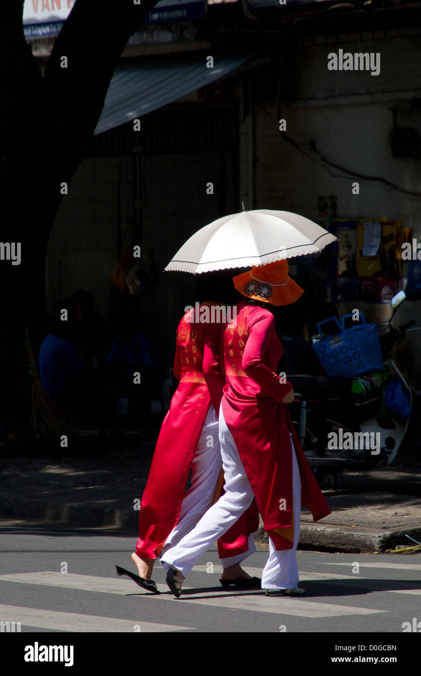 Deux femmes en costume traditionnel de traverser une rue à Ho Chi Minh Ville au Vietnam. Banque D'Images