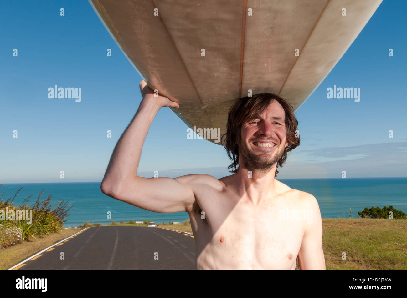 Homme debout avec surfer longboard sur le dessus de la tête avec la combinaison jusqu'à sa taille, Raglan Nouvelle-zélande. Banque D'Images