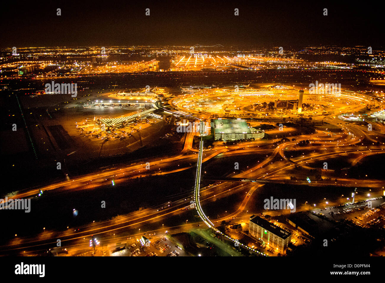 NEWARK, New Jersey, États-Unis — une vue aérienne de l'aéroport international Liberty de Newark (EWR) de nuit, capturée depuis un hélicoptère à environ 500 pieds d'altitude, révèle l'immense complexe terminal illuminé dans l'obscurité. Le système de monorail Airtrain est clairement visible sous la forme d'une chaîne de lumières blanches s'étendant du centre au bas du cadre, mettant en valeur l'infrastructure de transport moderne de l'aéroport. Remarque : un bruit ISO élevé est visible en pleine résolution en raison des conditions de faible luminosité difficiles de la photographie aérienne nocturne. Banque D'Images