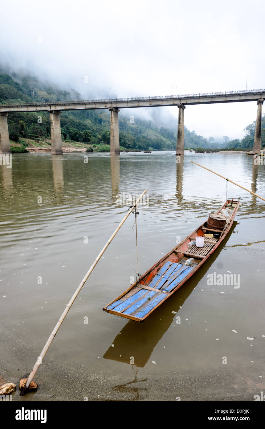 NONG KHIAW, Laos - un bateau en bois est mouillée par des perches en bambou au bord de la Nam Nong Khiaw Ou in dans le nord du Laos. Banque D'Images