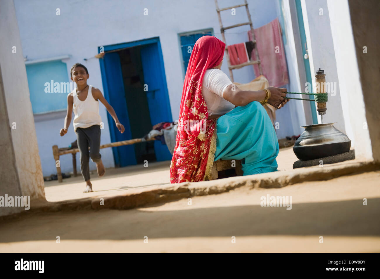 Femme le barattage du beurre avec son fils jouant derrière elle, Farrukh Nagar, Gurgaon, Haryana, Inde Banque D'Images