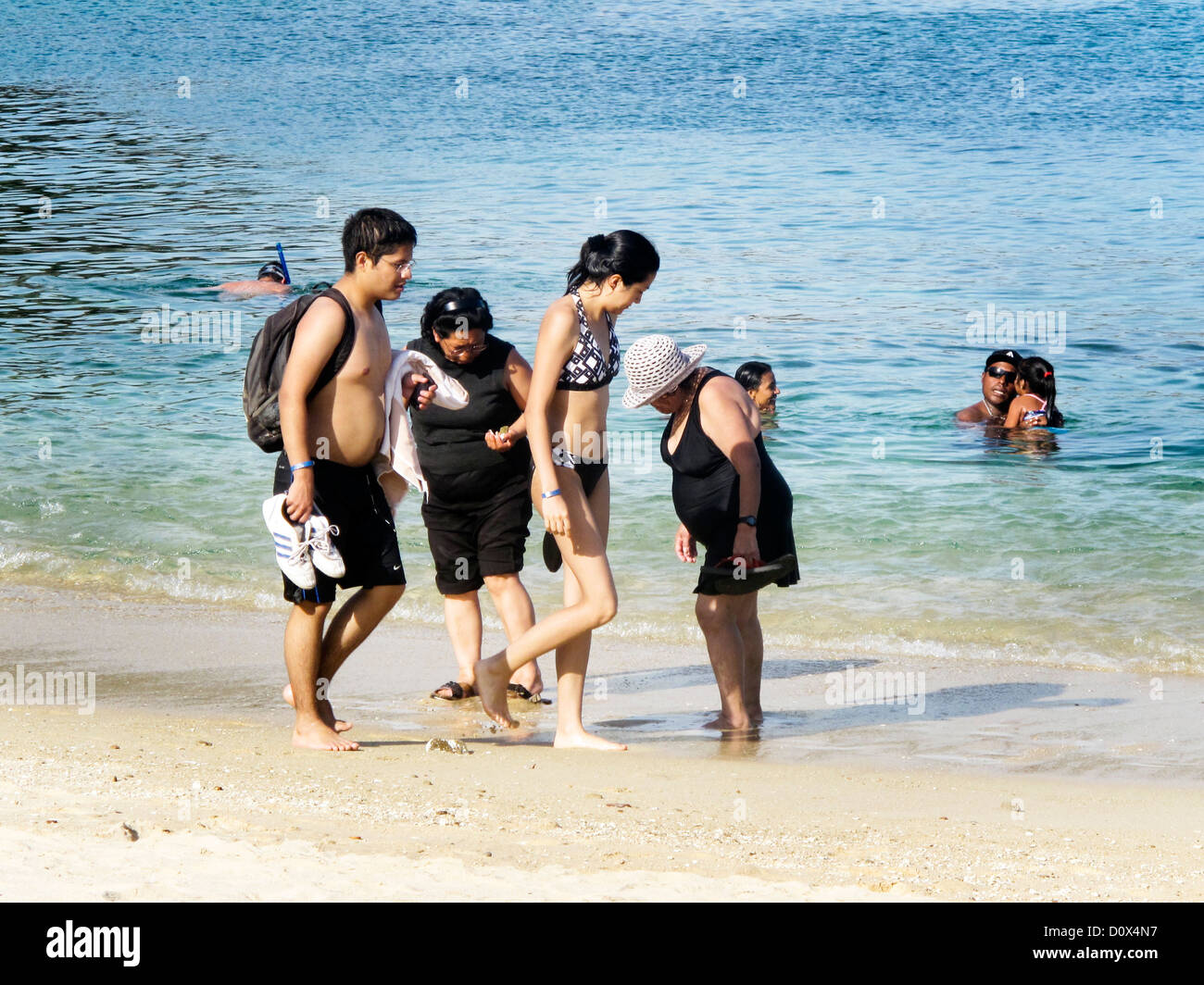 Jeune couple mexicain passe 2 dumpy collecte des femmes plus âgées, à bord de l'eau que d'autres amateurs de plage profiter de la mer bleu translucide Banque D'Images