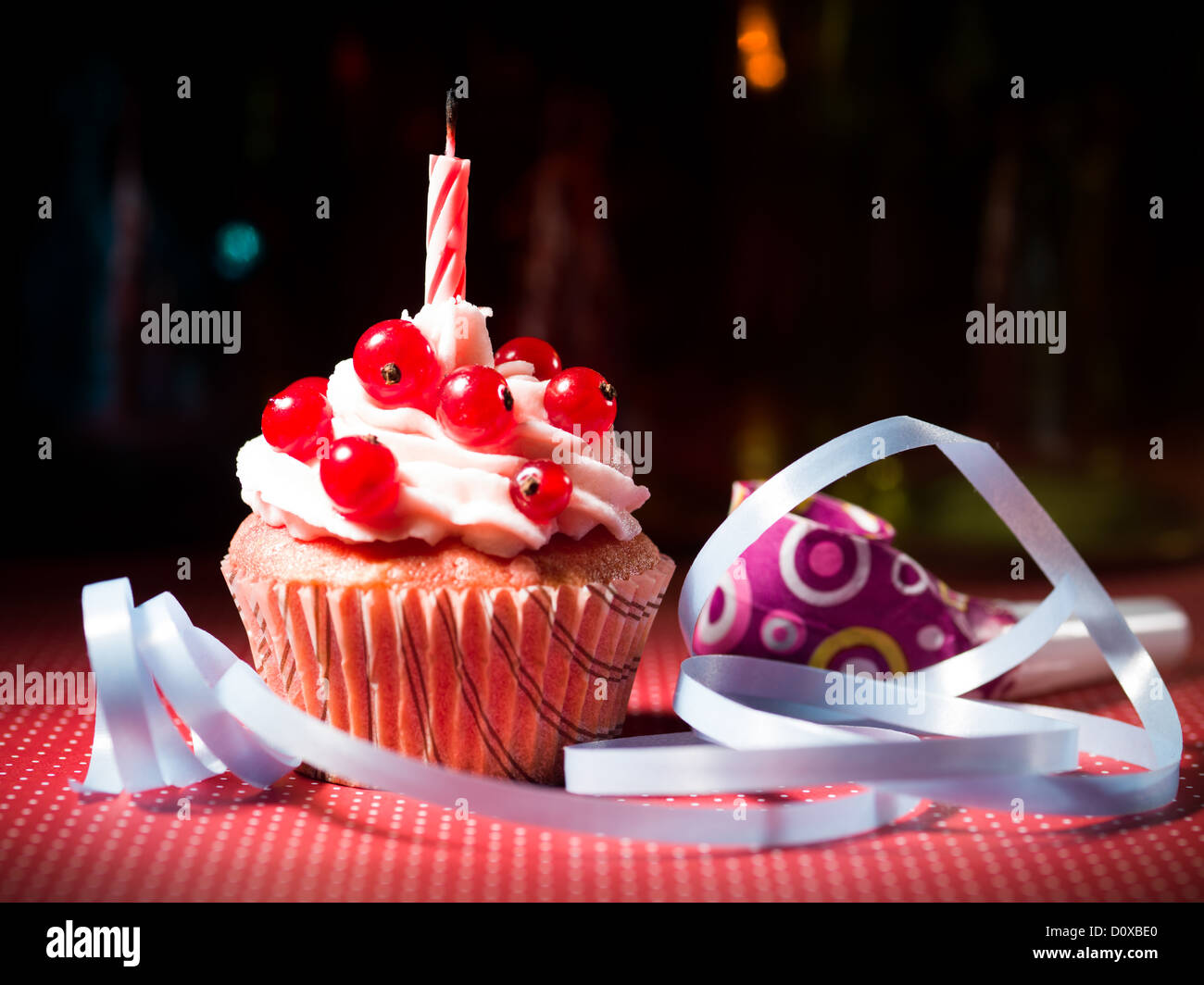 Muffin aux bleuets avec bougie soufflée sur la table avec des rubans des décorations en pointillé rouge et bleu et fond coloré Banque D'Images