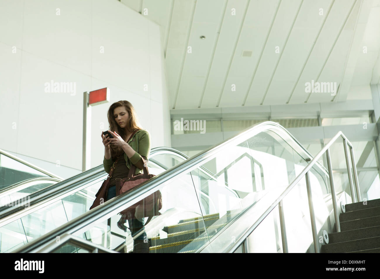Jeune femme sur smartphone à l'aide d'escalator Banque D'Images