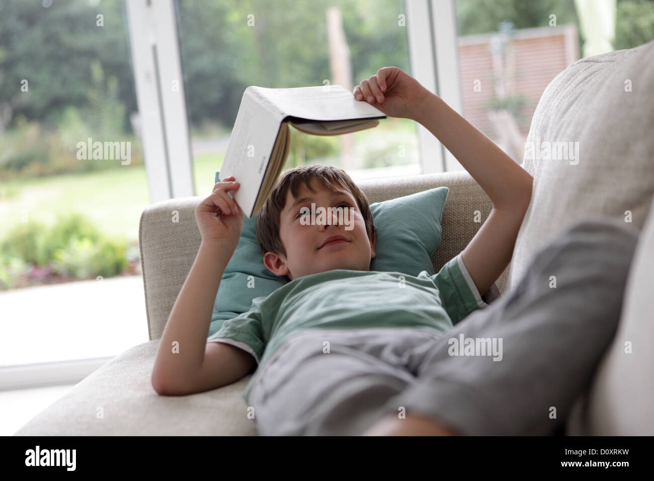 Garçon couché sur le canapé et la lecture d'un livre Banque D'Images