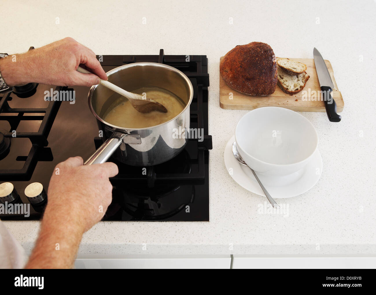 L'homme en remuant la casserole de soupe sur une plaque de cuisson Banque D'Images