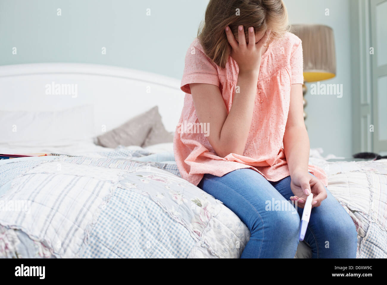 Teenage girl sitting on bed avec test de grossesse Banque D'Images