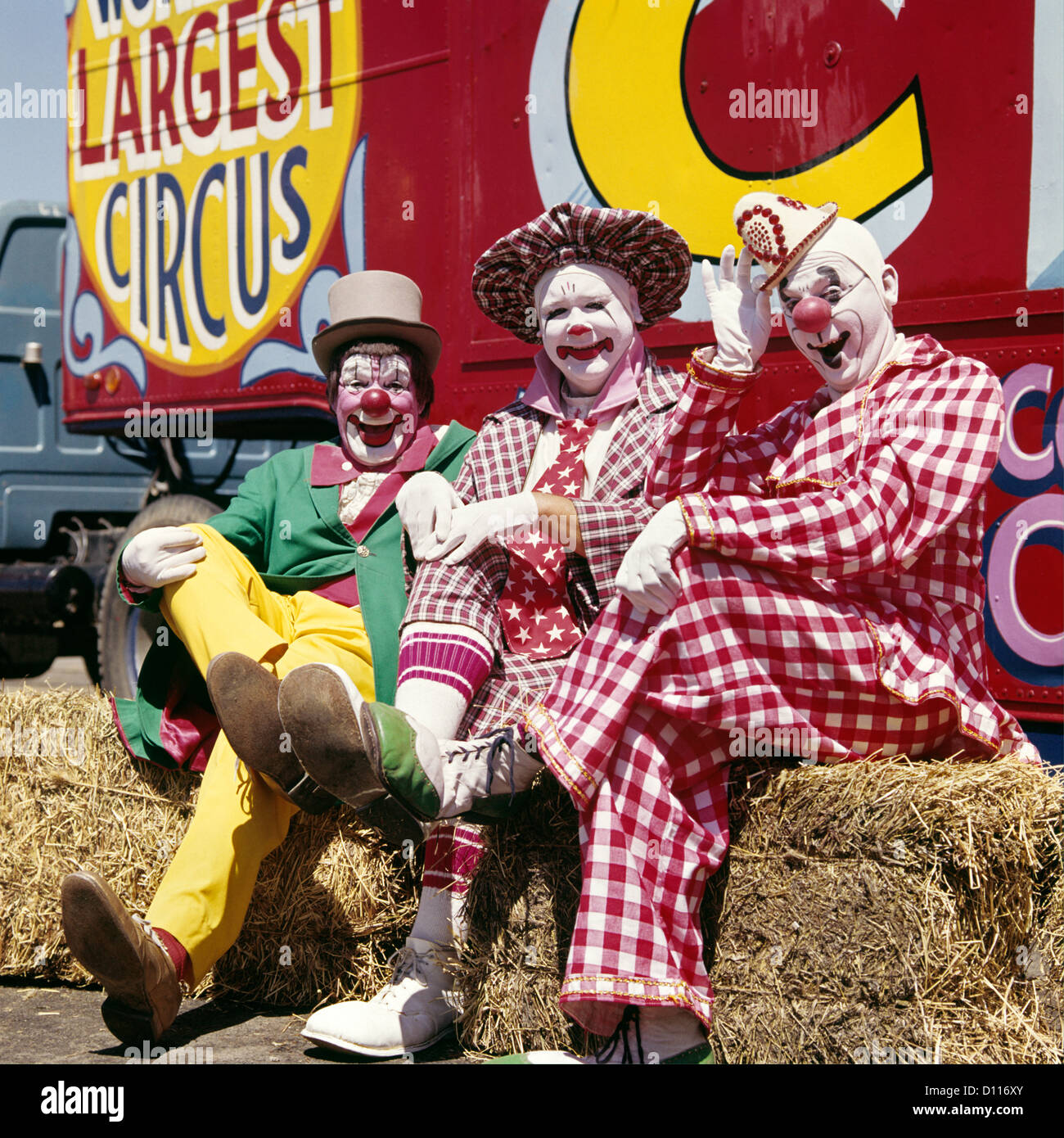 1970 THREE LAUGHING CLOWNS ASSIS SUR DES BALLES DE FOIN PAR CIRCUS WAGON LOOKING AT CAMERA Banque D'Images