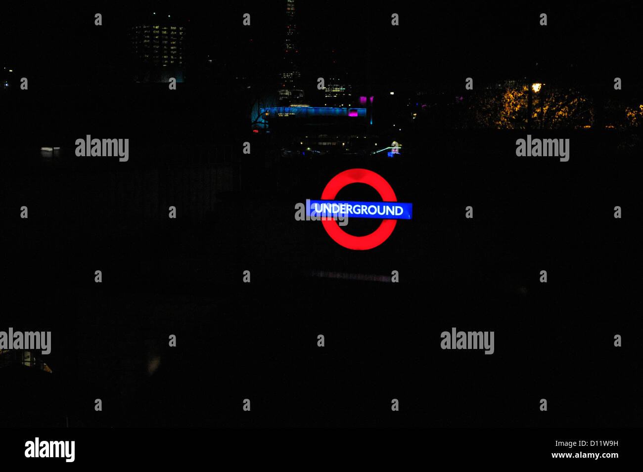 London Underground tube lumineux, signe avec fond sombre pour copier l'espace. Des lueurs de la ville la nuit derrière. Banque D'Images