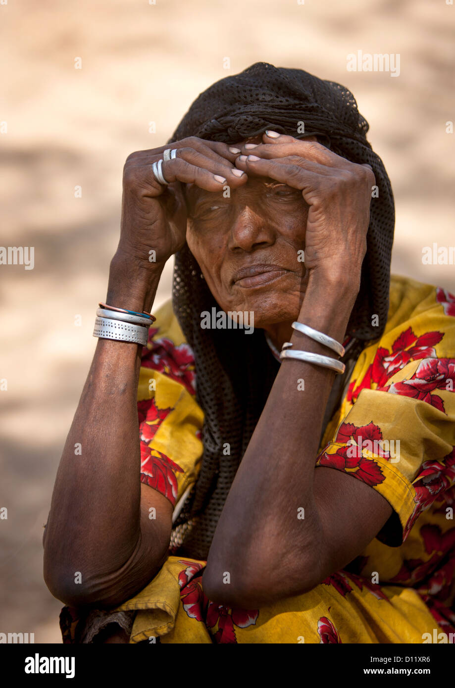 Portrait d'une ancienne tribu Karrayyu femme accroupie et à protéger ses yeux du soleil, Metahara, Ethiopie Banque D'Images