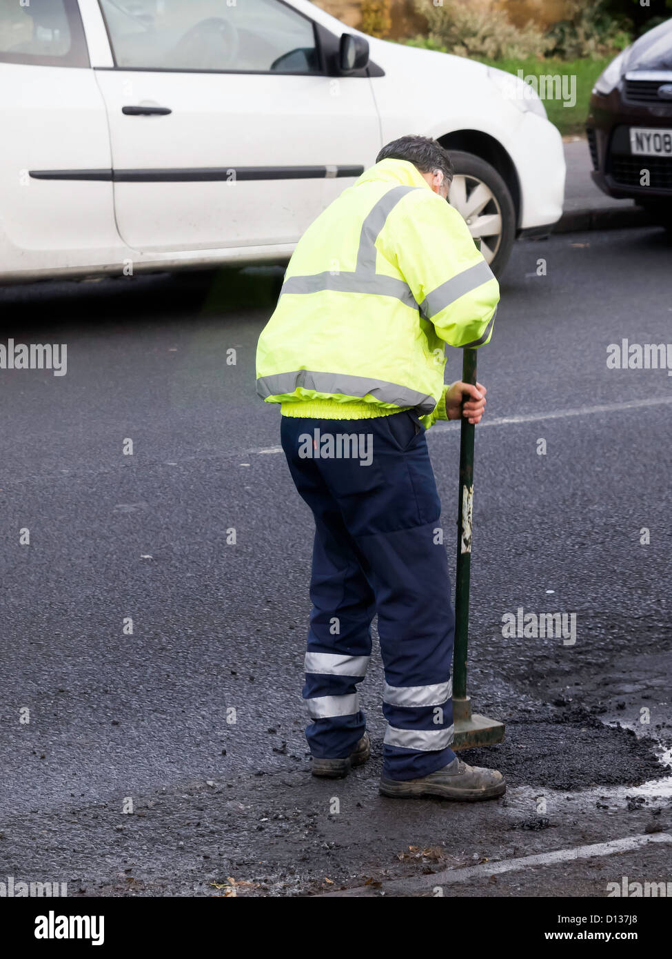 L'autorité locale de la réparation des routes man making une réparation temporaire à un nid de poule sur une route très fréquentée Banque D'Images