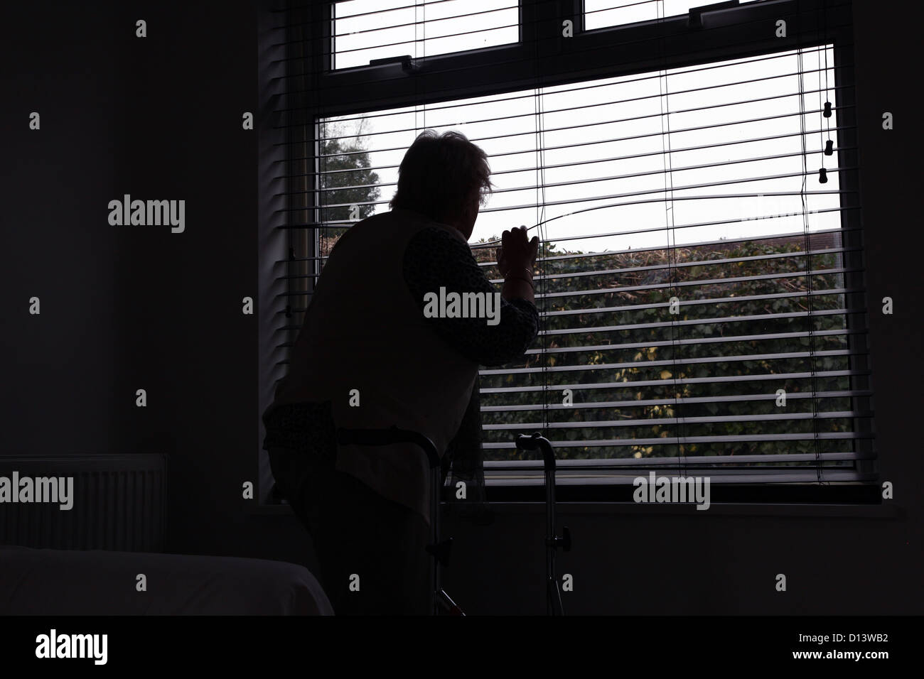 Hauts femme avec un déambulateur à la fenêtre d'un aveugle. Vue arrière, silhouette. Banque D'Images