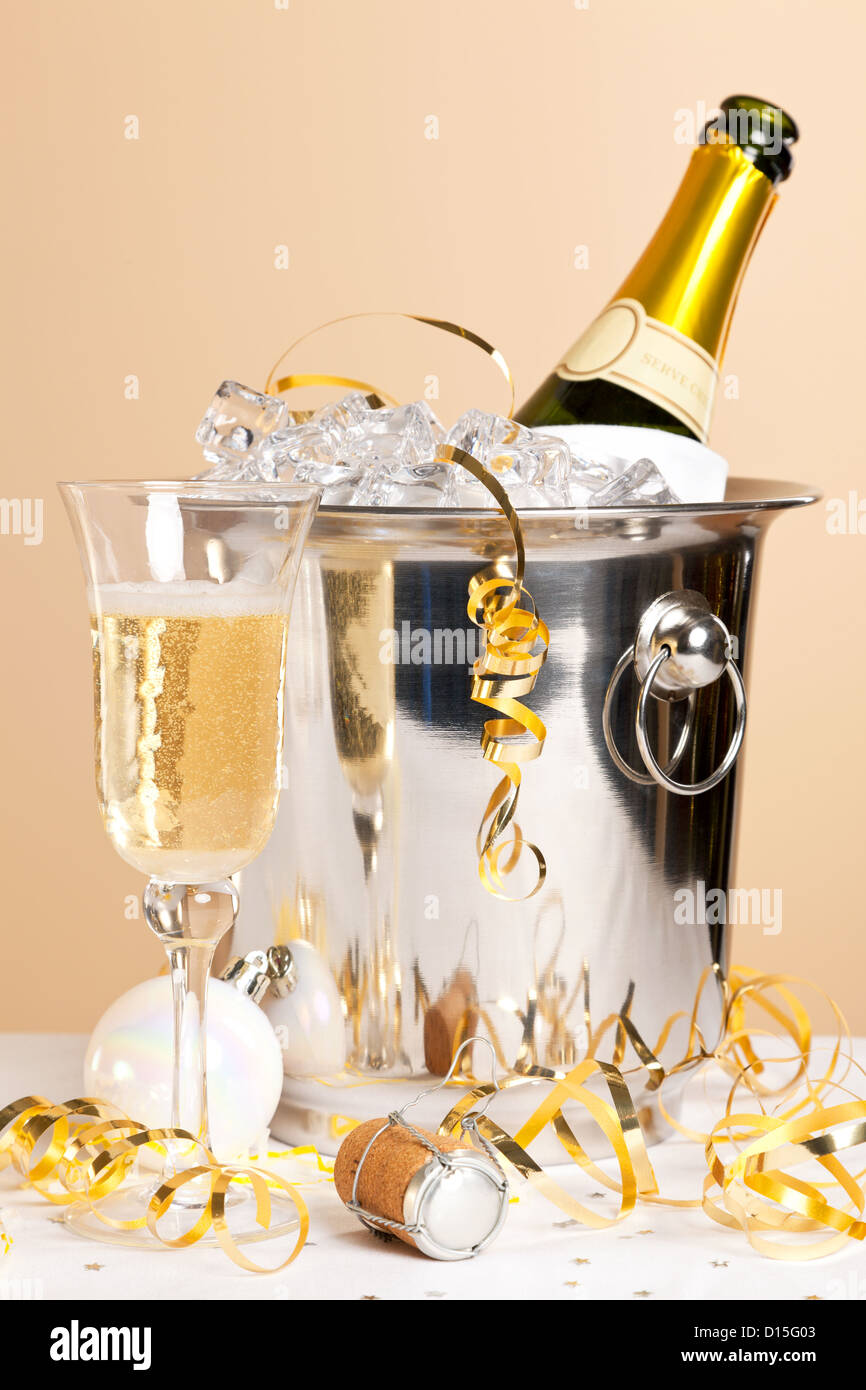 Un verre de champagne avec une bouteille dans un seau à glace et banderoles d'or à travers la table Banque D'Images