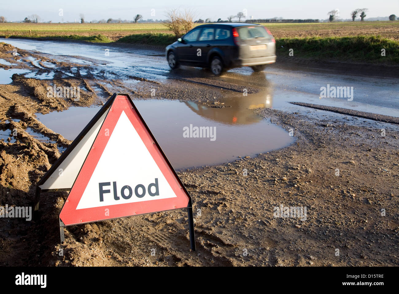 Un avertissement de crue en regard de la route avec les eaux de crue juste derrière, et une Ford Focus break s'approche de la montée des eaux. Banque D'Images